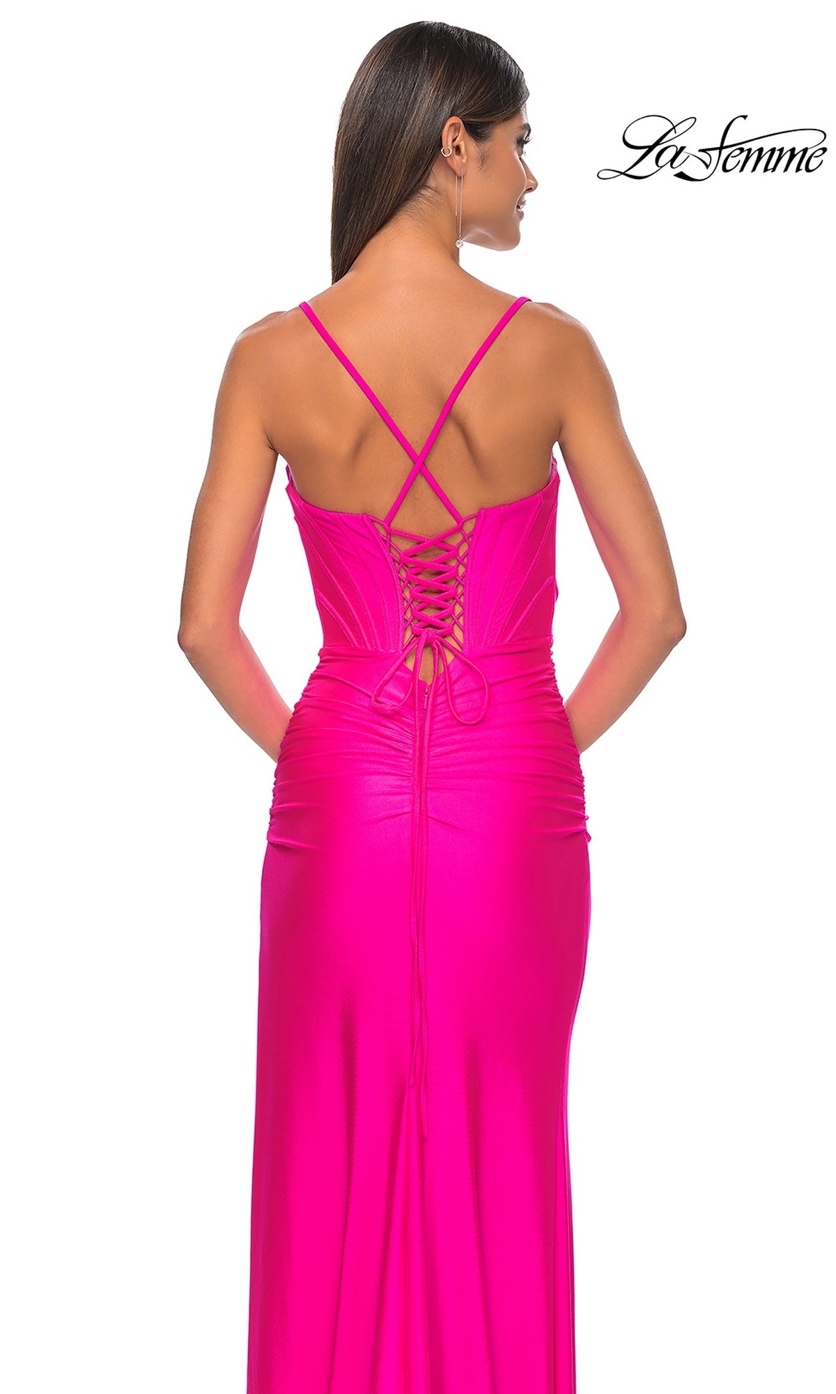 Woman wearing the La Femme Long Bustier-Bodice Prom Dress 32256 in bright pink, featuring crisscrossed straps, a corset-style bodice, and lace-up back, standing against a white background.